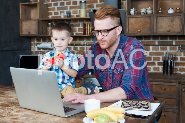 自宅で息子の世話をしながら仕事するお父さん 自宅で息子の世話をしながら仕事するお父さんの写真