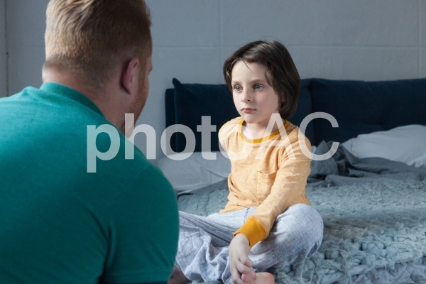 ベッドに座る子供の話を聞くお父さん2 ベッドに座る子供の話を聞くお父さん2の写真
