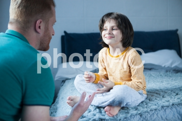 ベッドに座る子供の話を聞くお父さん3 ベッドに座る子供の話を聞くお父さん3の写真