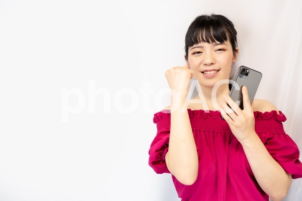 スマホを持ってガッツポーズをする女性(白背景) スマホを持ってガッツポーズをする女性(白背景)の写真