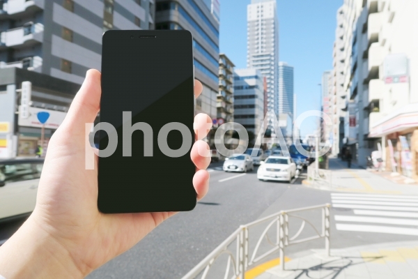 歩きスマホをする男性の手と街並み 歩きスマホをする男性の手と街並みの写真