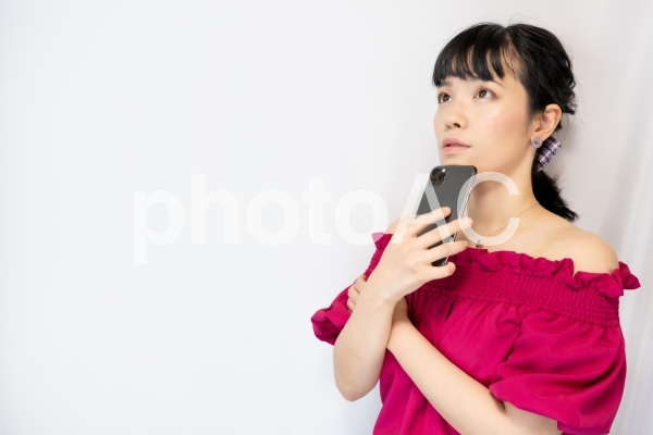 スマホを持って考える女性(白背景) スマホを持って考える女性(白背景)の写真